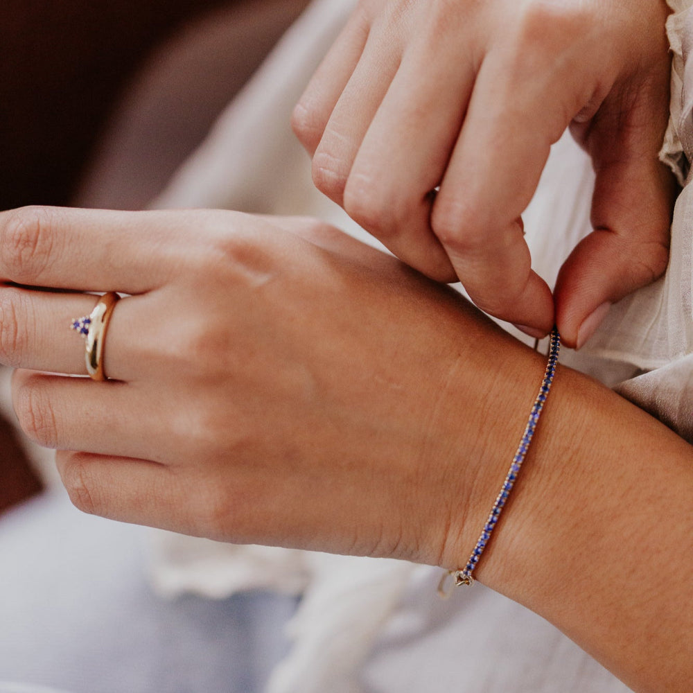 Close-up of hands with a bracelet and ring, wearing a light-colored garment.
