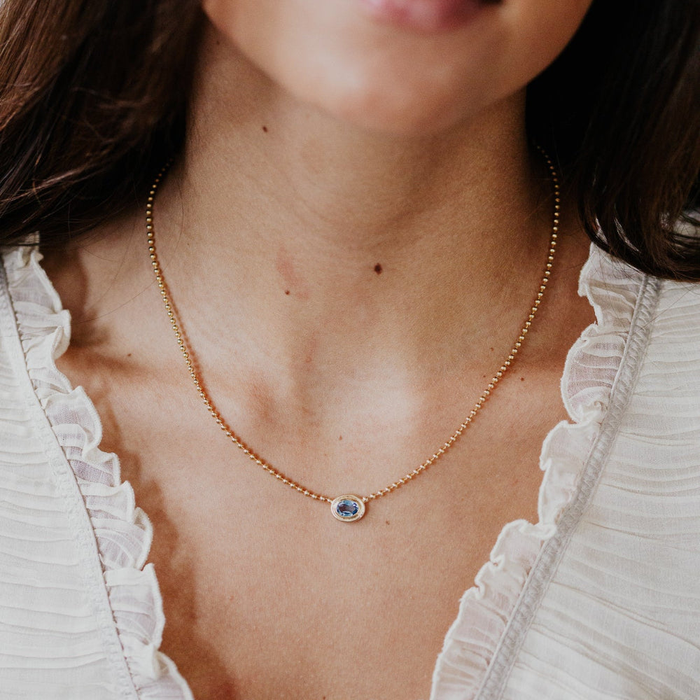 Close-up of a person wearing a gold necklace with a blue gemstone pendant.