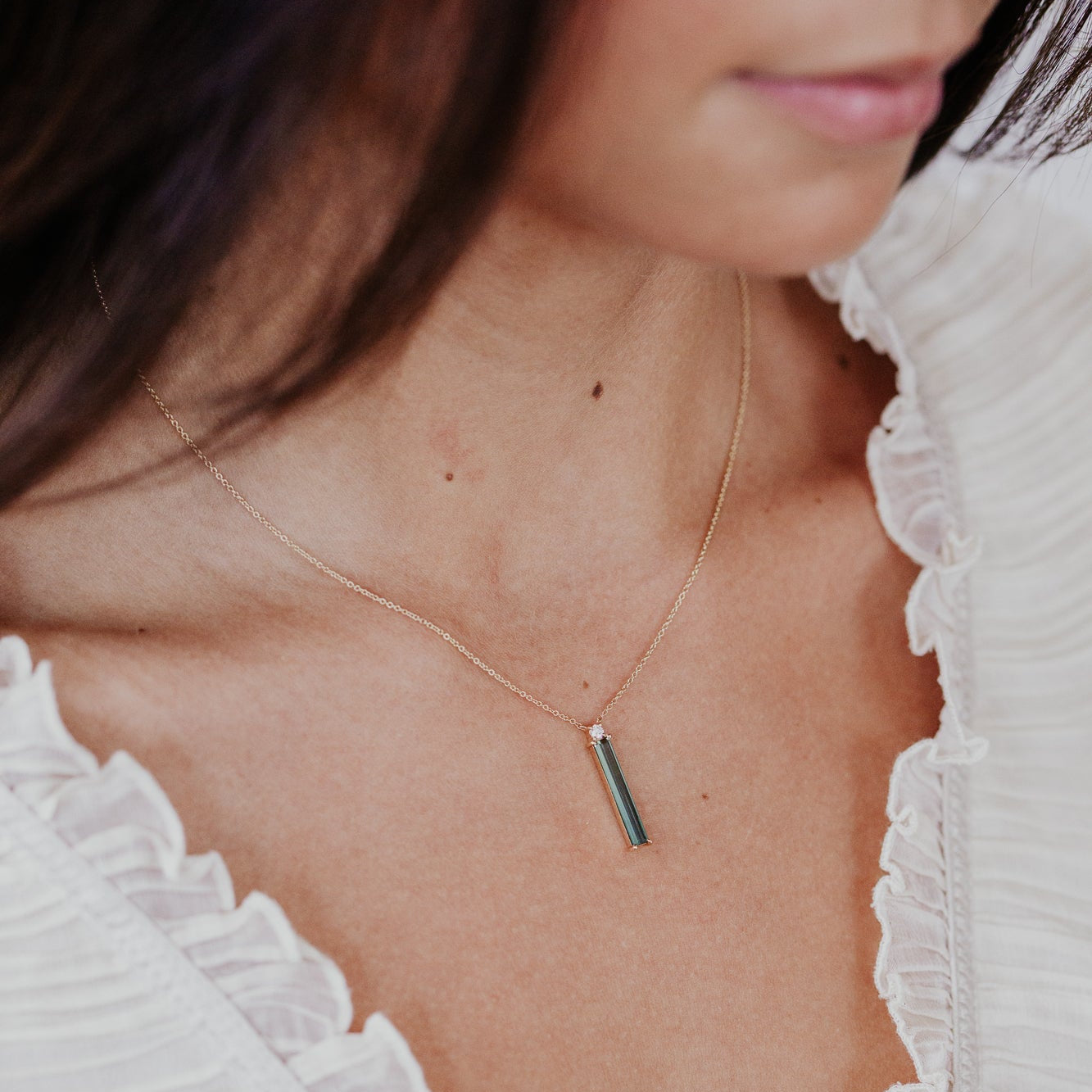 Close-up of a person wearing a delicate necklace with a green tourmaline pendant.