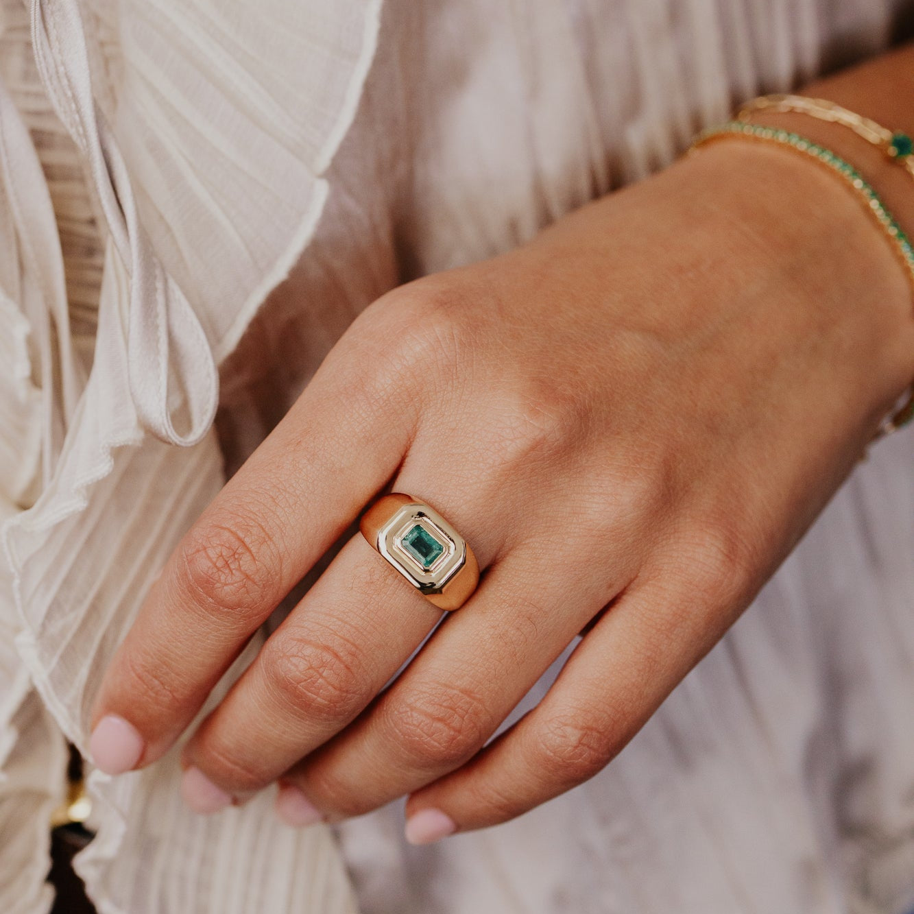 Hand wearing a ring with a green emerald gemstone, blurred background