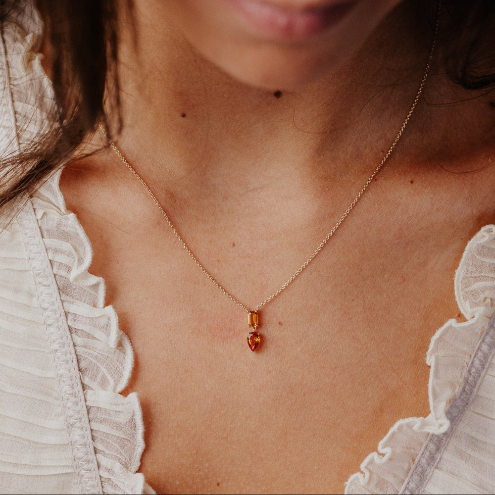 Close-up of a person wearing a delicate necklace with a  citrine  pendant.