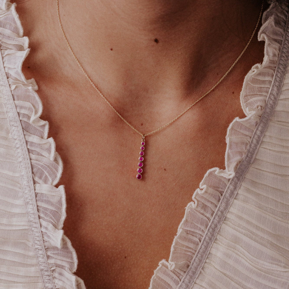Close-up of a person wearing a delicate necklace with a pink ruby pendant.