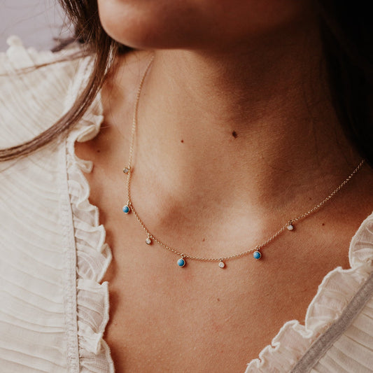 Close-up of a woman wearing a delicate necklace with turquoise and diamonds