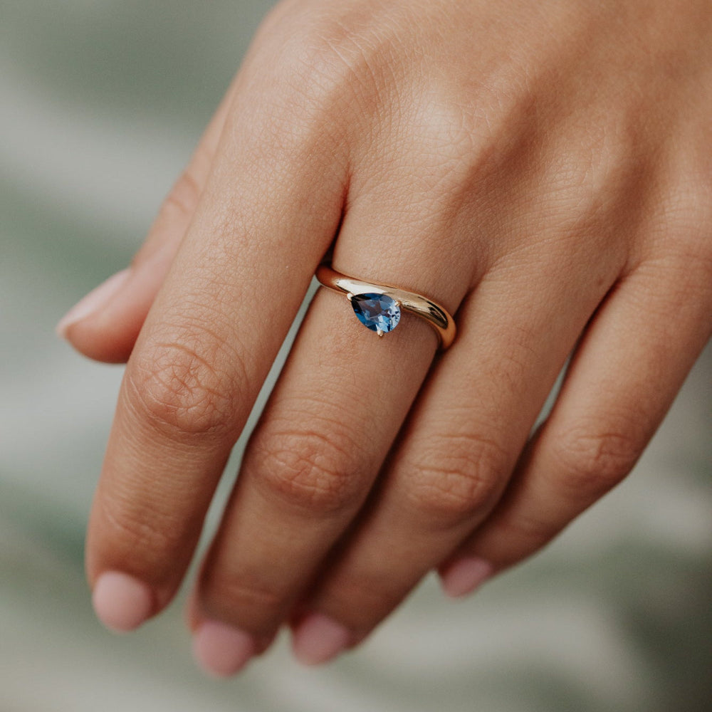 Hand wearing a gold ring with a blue gemstone on a blurred background
