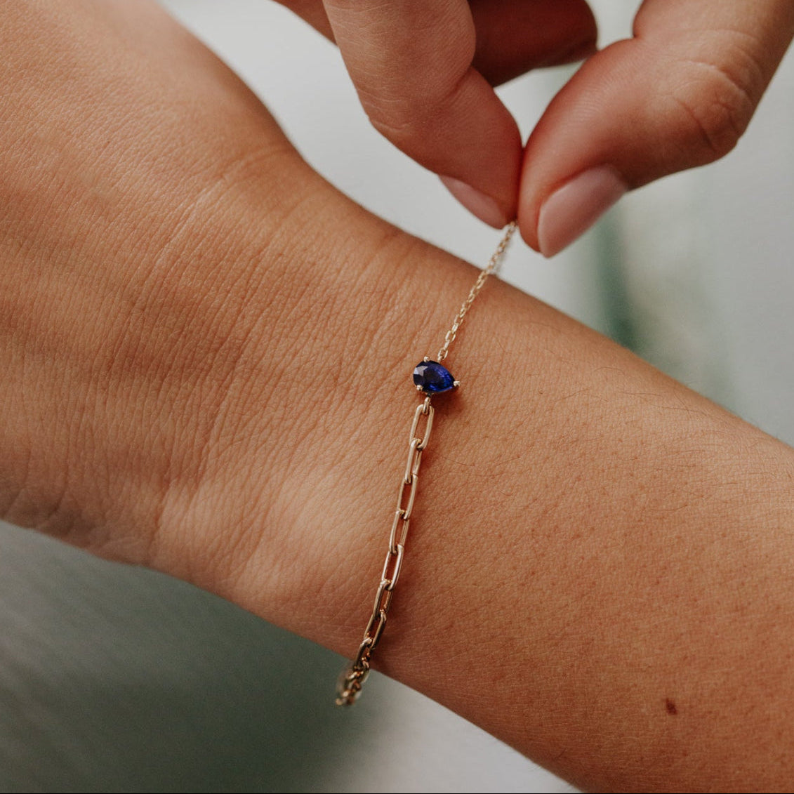 Gold bracelet with a blue sapphire gemstone on a wrist against a neutral background
