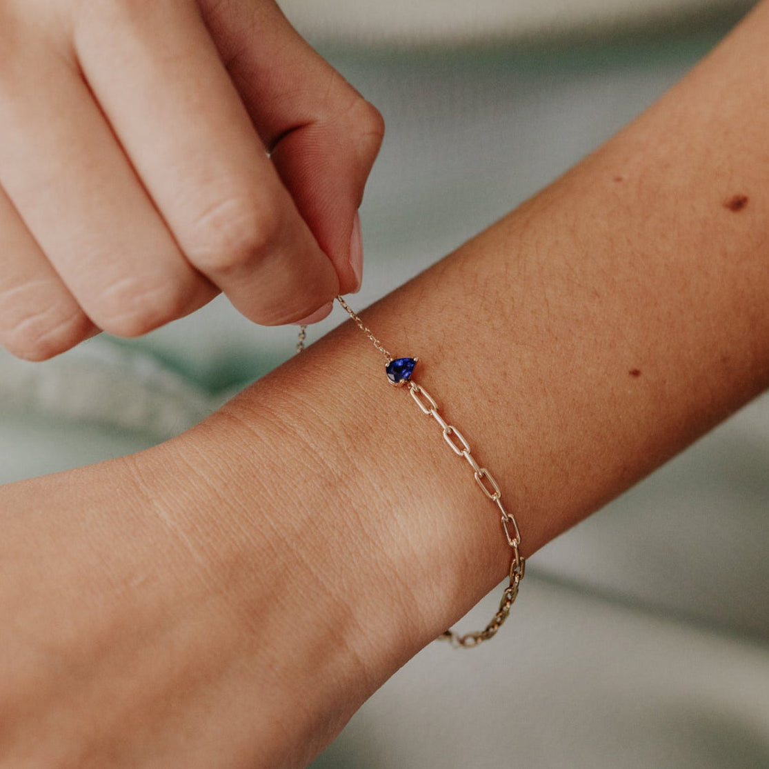 Person wearing a delicate gold bracelet with a blue sapphire gemstone on a blurred background