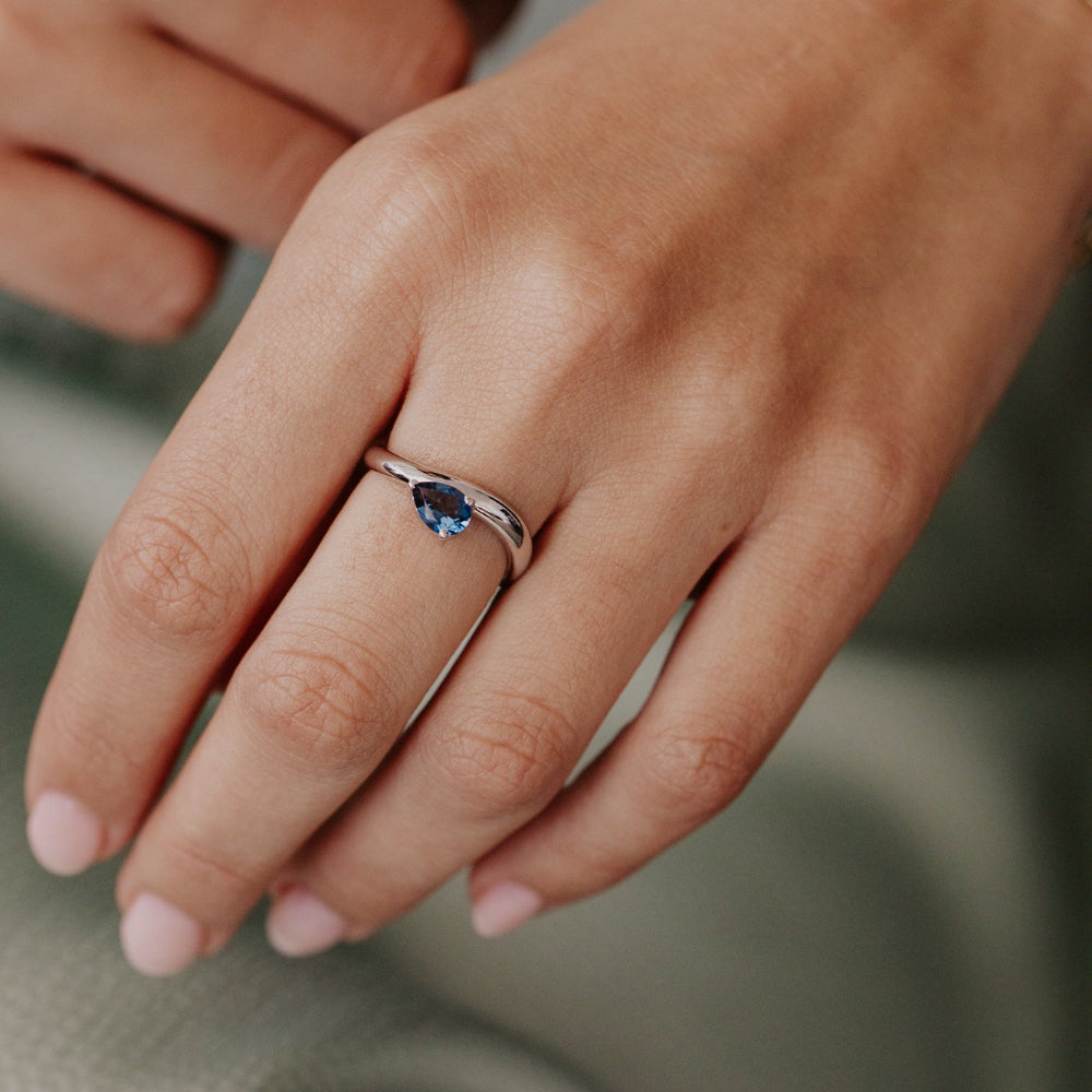 Close-up of a hand wearing a ring with a blue gemstone on a blurred background