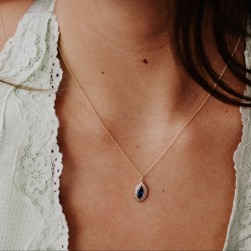Close-up of a person wearing a delicate London blue topaz necklace with a blue pendant.
