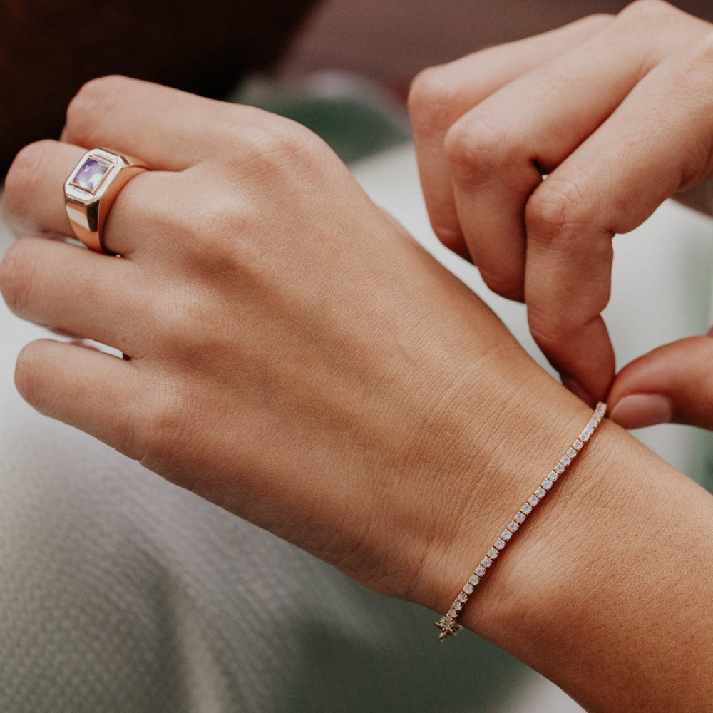 Close-up of a hand wearing a rose gold ring and bracelet with a blurred background