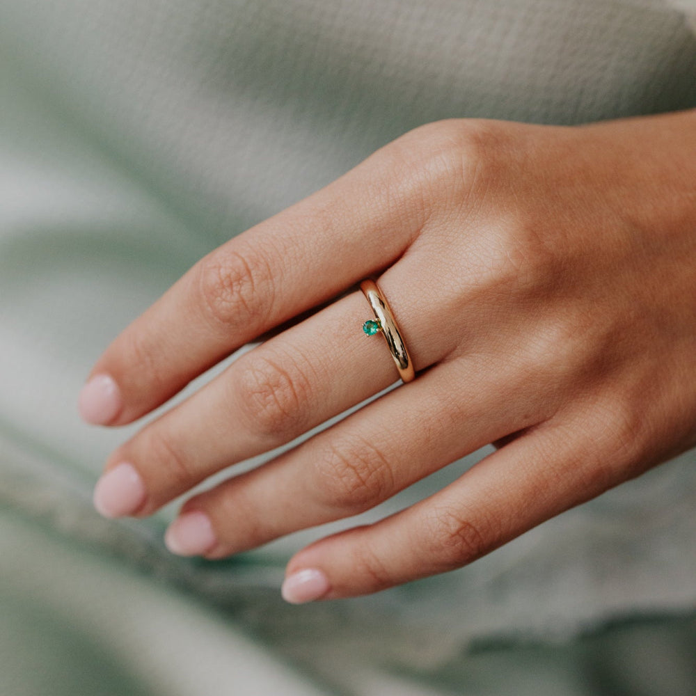Hand wearing a gold ring with a green gemstone against a blurred background