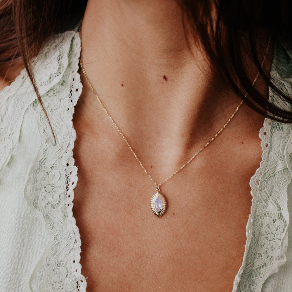 Close-up of a person wearing a delicate moonstone necklace with a teardrop pendant.