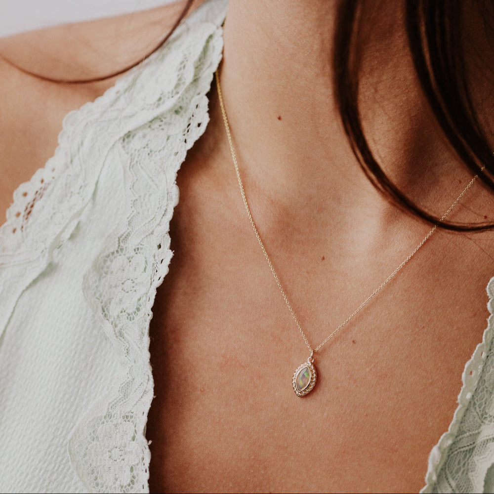 Close-up of a gold necklace with a opal pendant on a person wearing a light green lace garment.