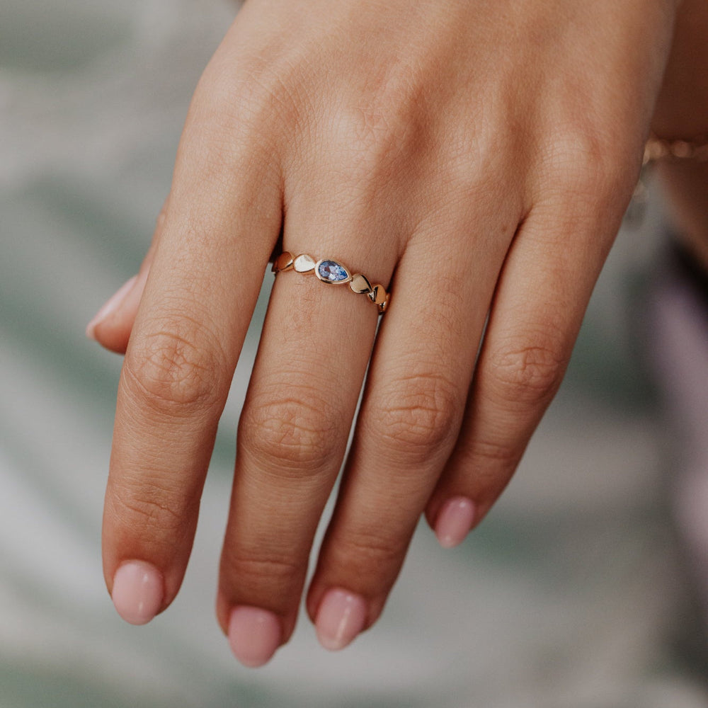 Close-up of a hand wearing a gold ring with a blue gemstone on a blurred background