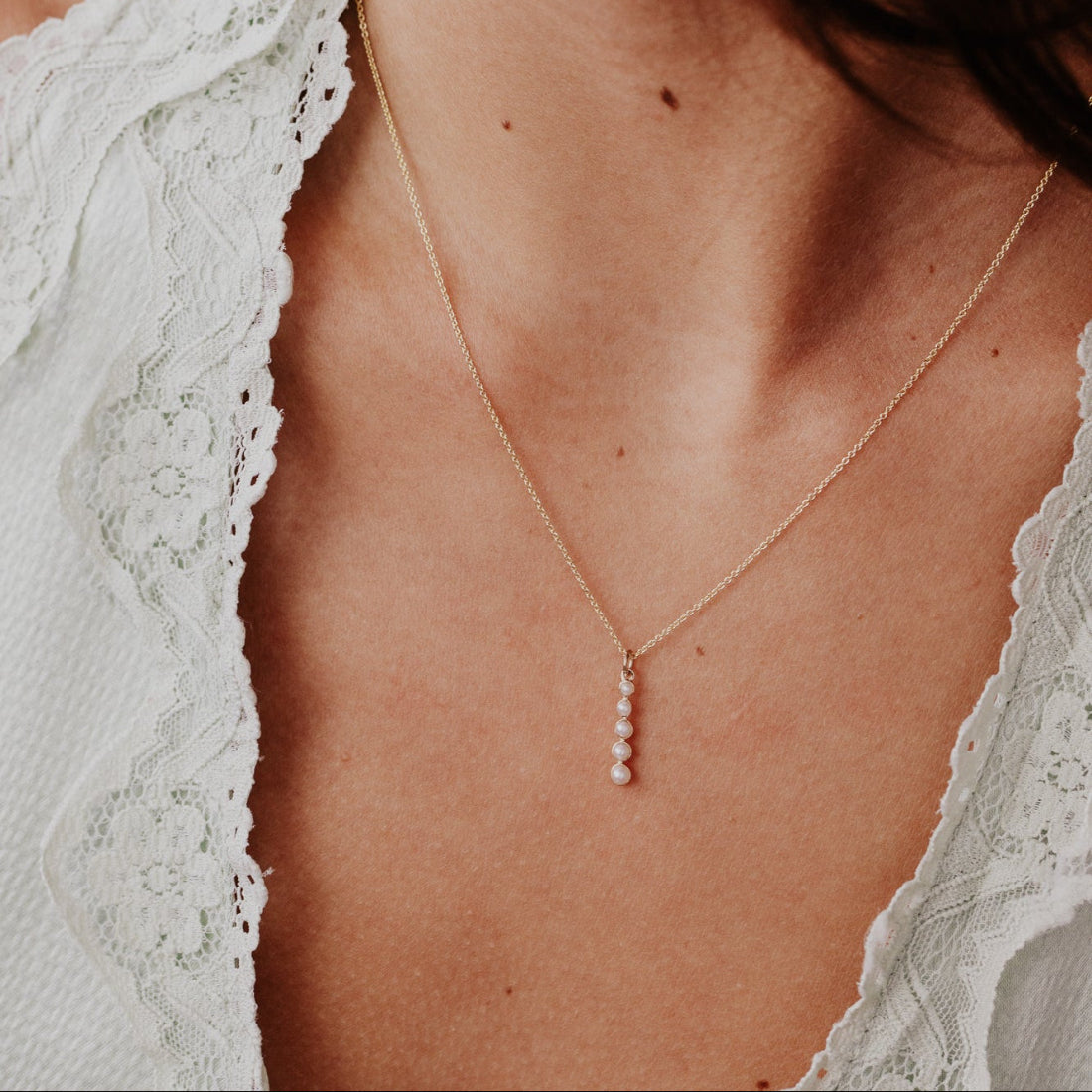 Close-up of a person wearing a delicate  pearl necklace with a blurred background