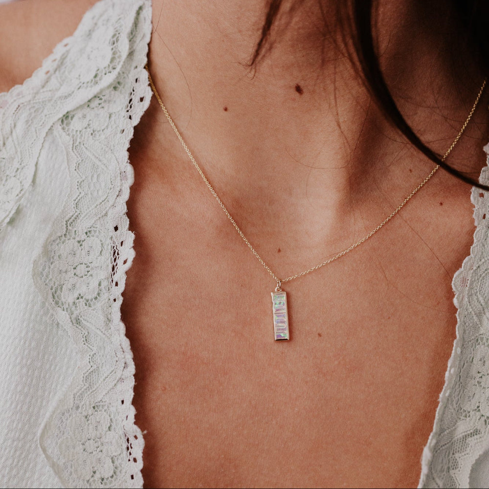 Necklace with a opal pendant worn by a person in a white lace garment.