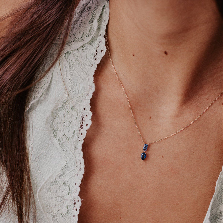 Close-up of a necklace with a blue topaz pendant on a person wearing a white lace garment.