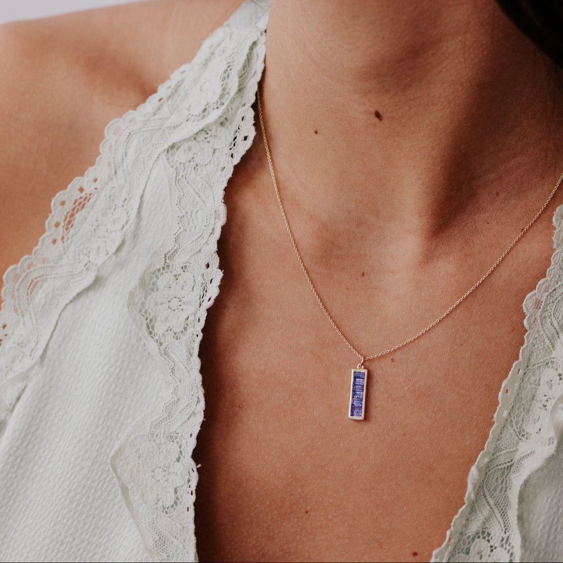 Necklace with a blue sapphire pendant worn by a person in a white lace garment.