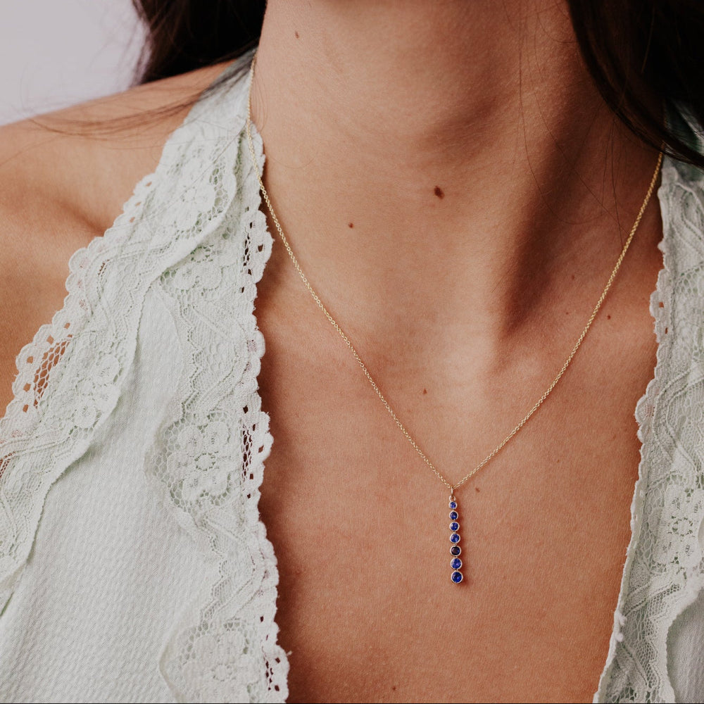 Necklace with a blue gemstone sapphire pendant worn by a person in a light-colored top.