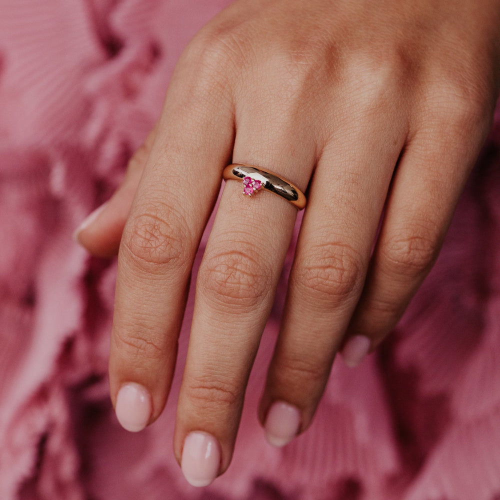 Hand wearing a ring with a ruby gemstone on a pink textured background