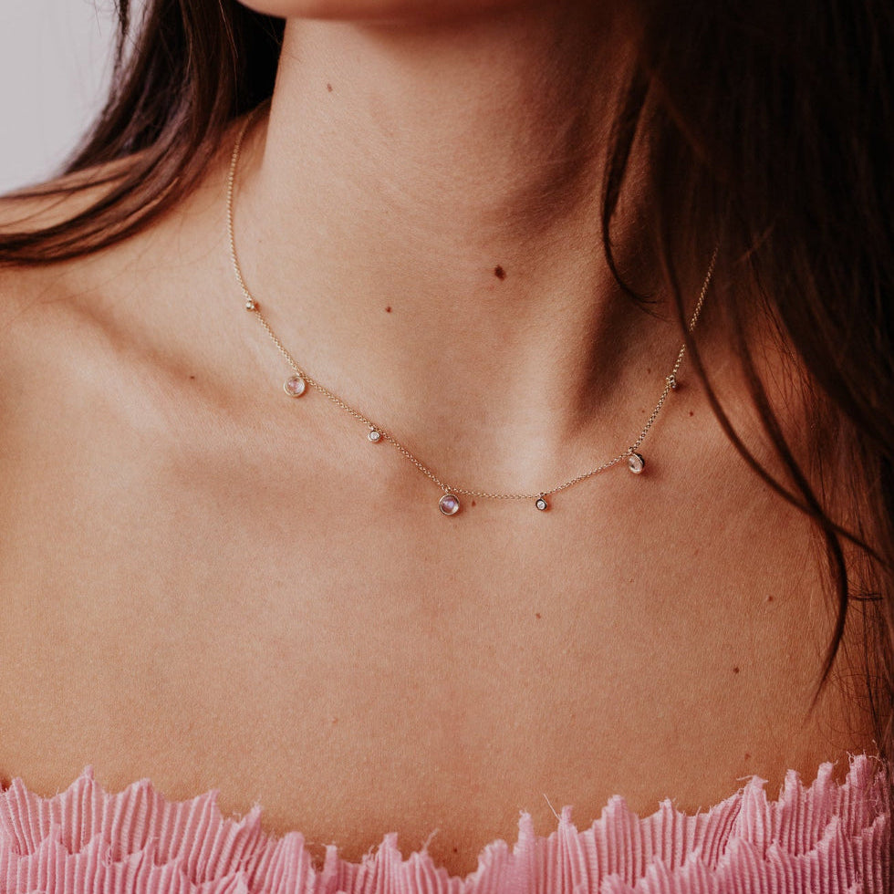 Necklace with moonstone and diamond pendants on a person wearing a pink top.