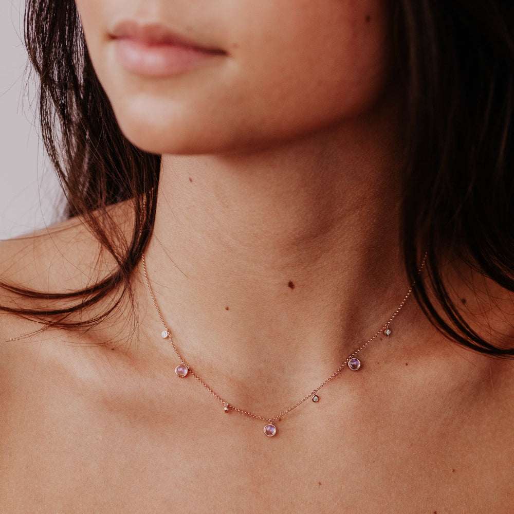 Close-up of a woman wearing a delicate moonstone and diamond necklace with a blurred background