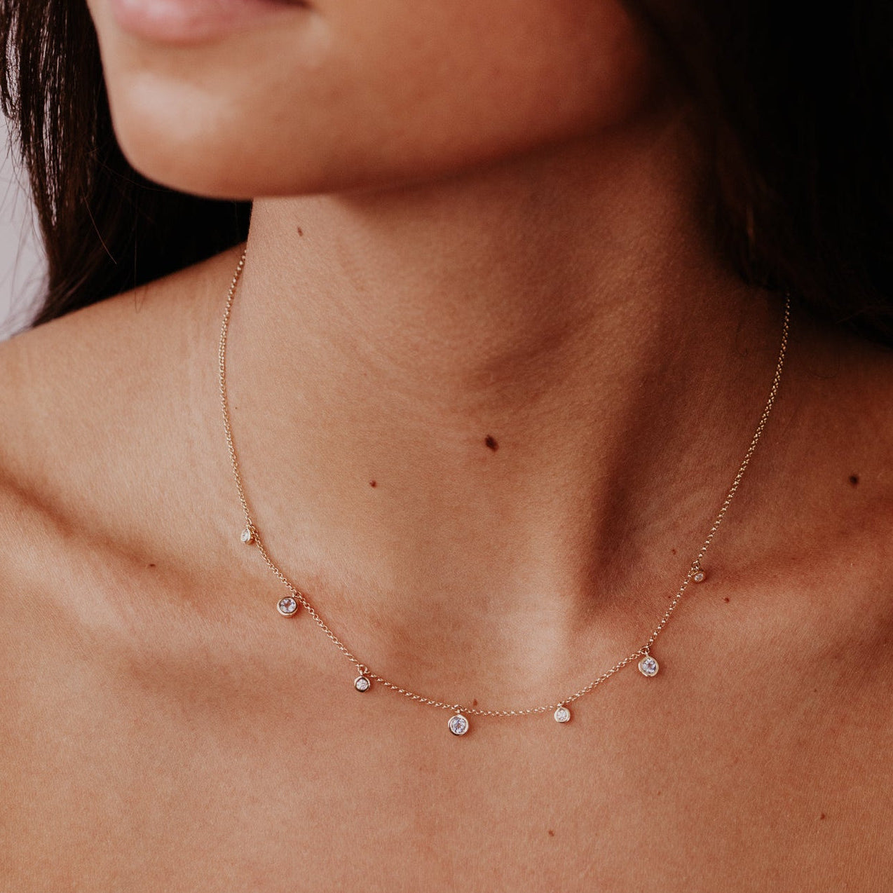 Close-up of a woman wearing a delicate aquamarine and diamond necklace with small beads.