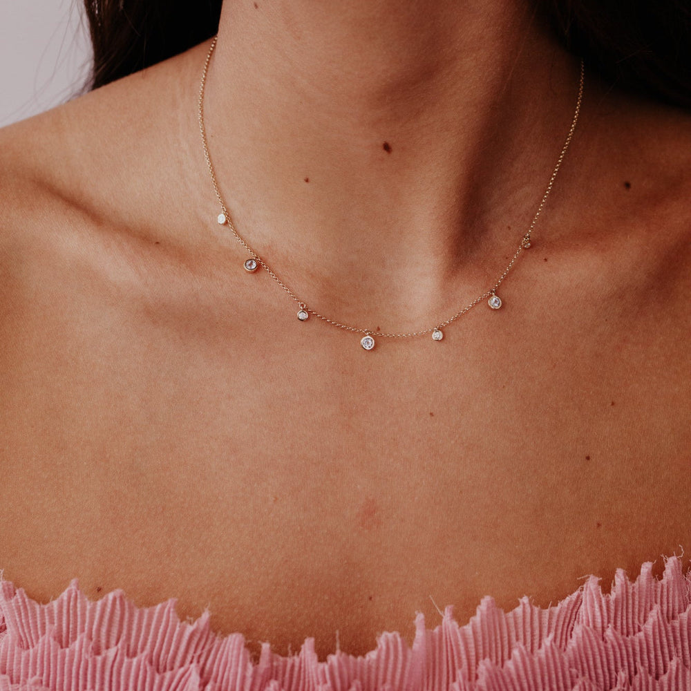 Close-up of a person wearing a delicate aquamarine and diamond necklace with a soft background