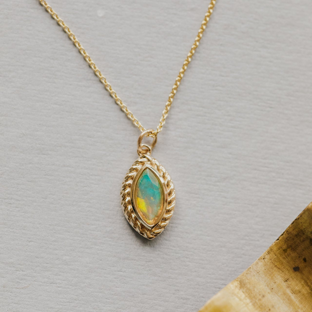 Gold necklace with a opal pendant featuring a turquoise stone on a gray background