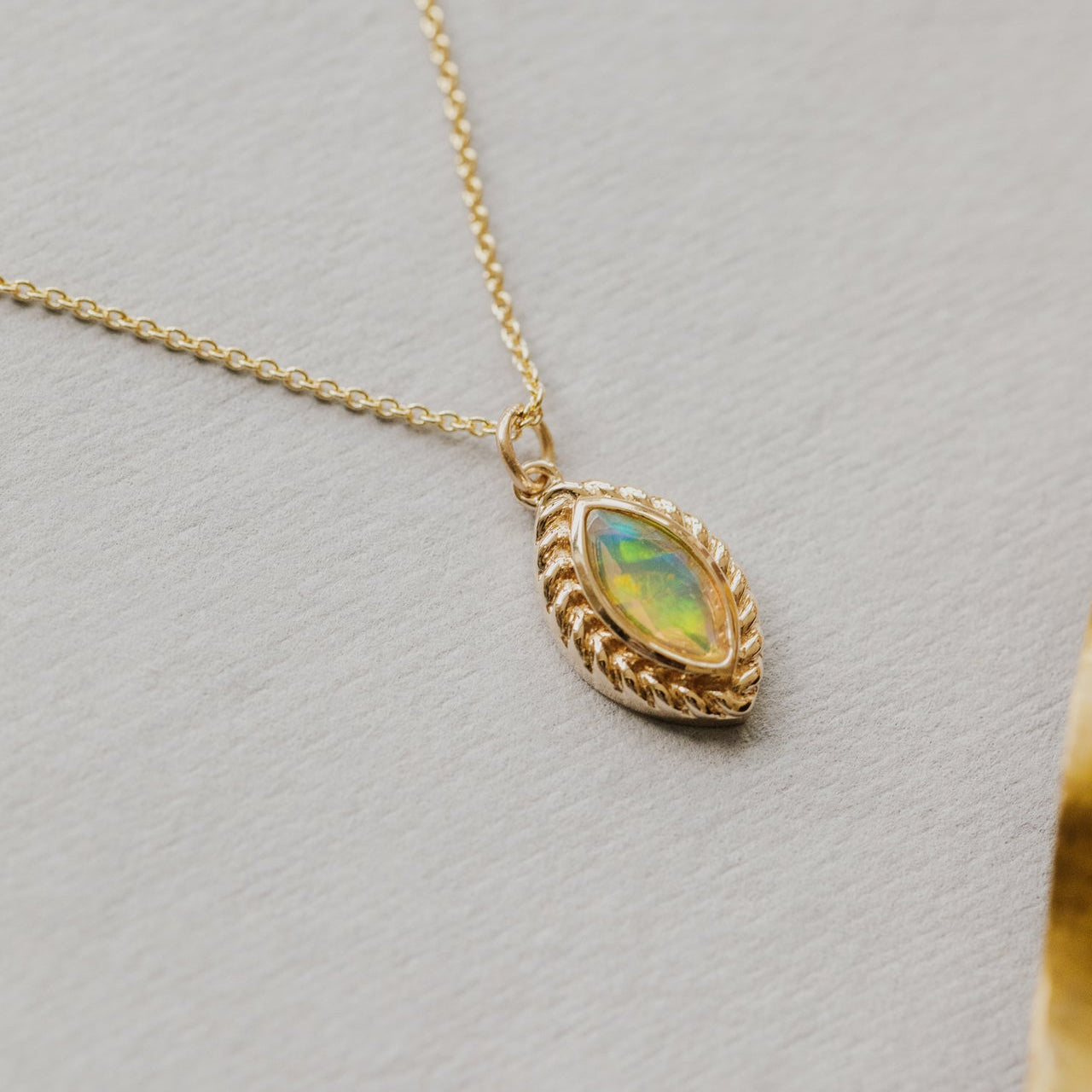 Gold necklace with an opal pendant on a light gray background
