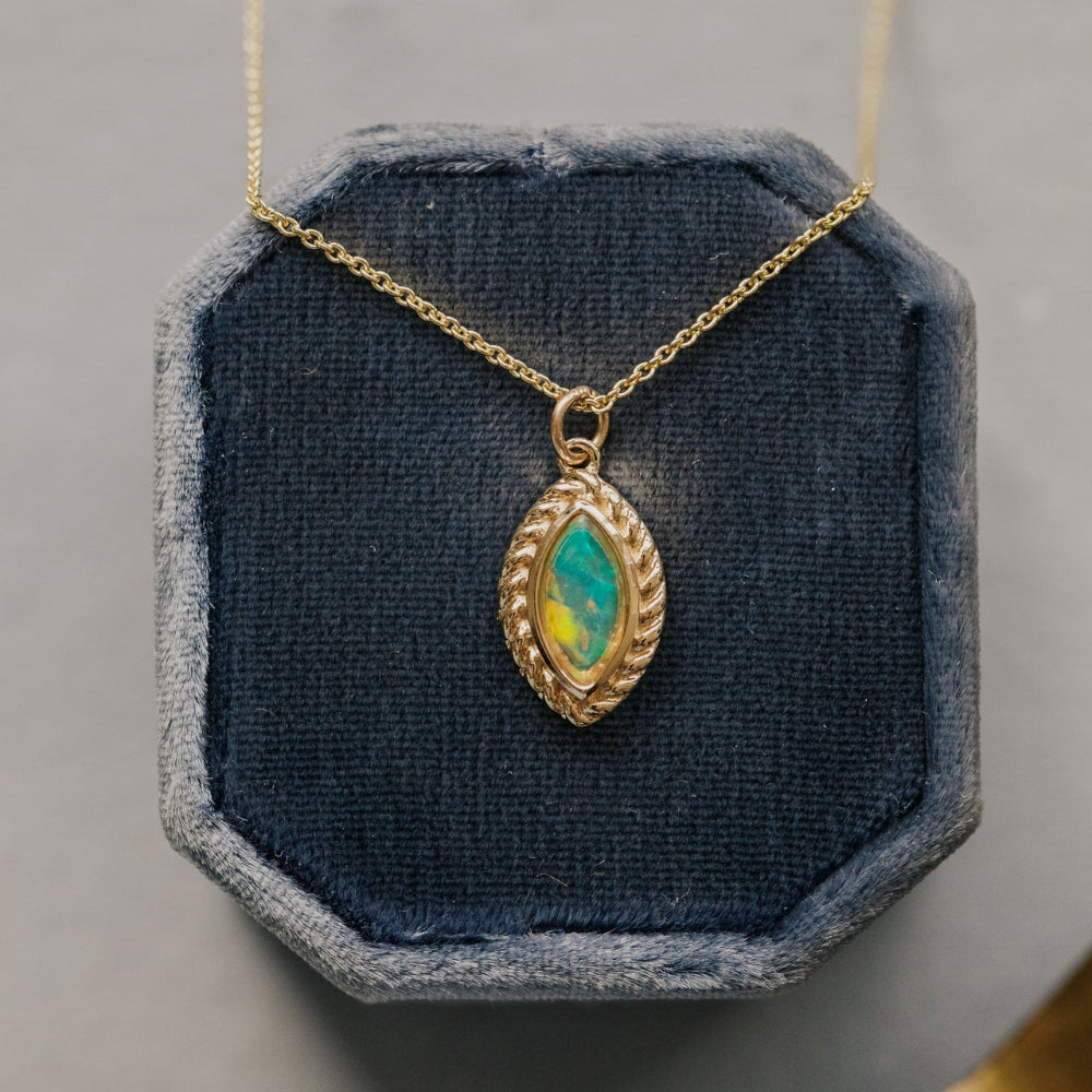Gold necklace with a green opal gemstone pendant on a blue cushioned stand.