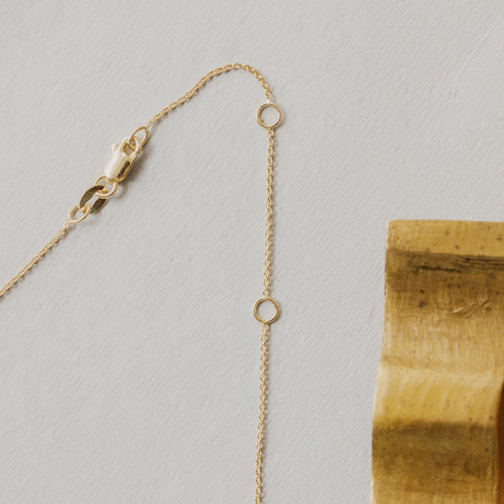 Gold necklace chain on a light gray background with a wooden block.