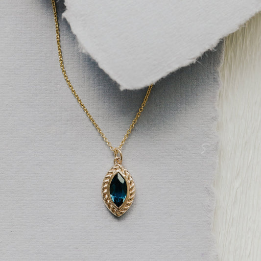 Gold necklace with a London blue topaz pendant on a textured gray background