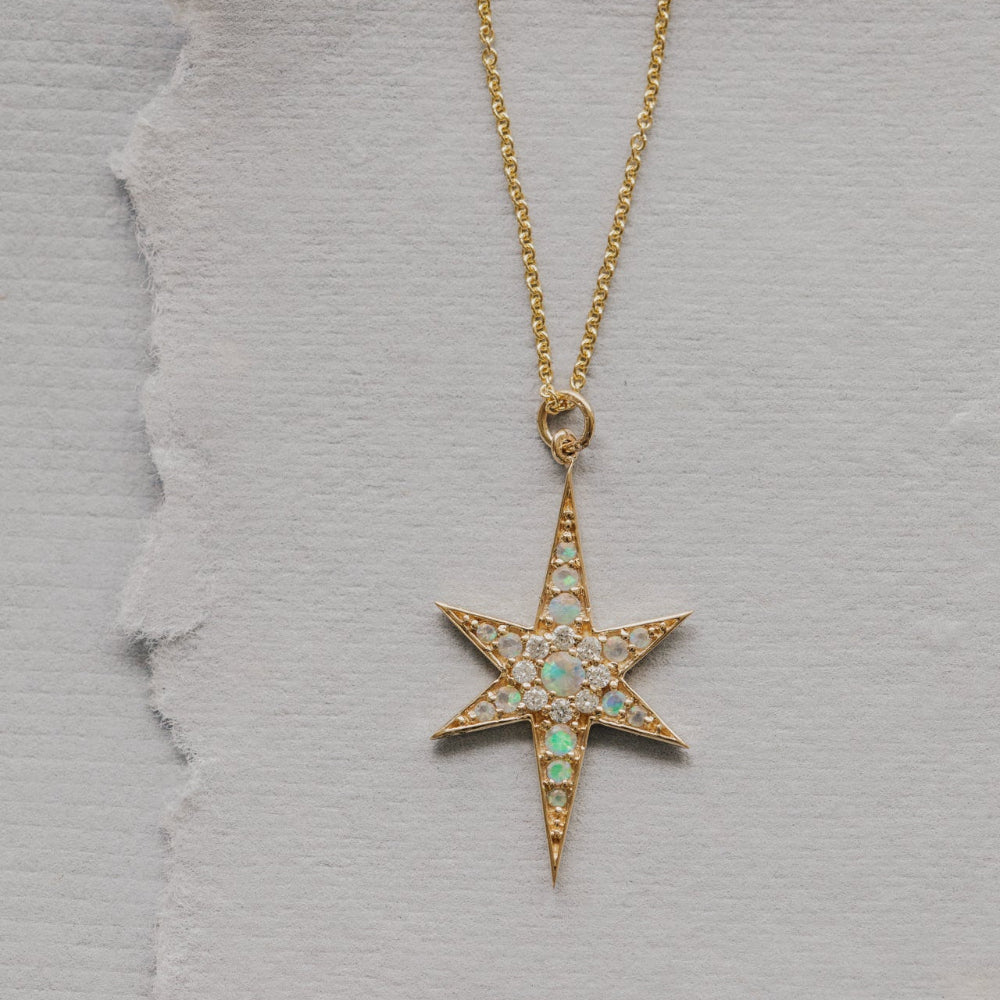 Star-shaped pendant necklace with opal and diamond gemstones on a gray textured background