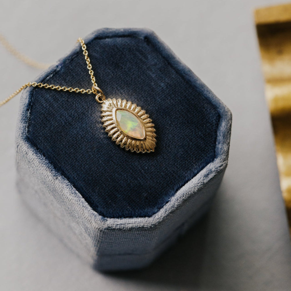 Gold necklace with a opal pendant on a blue hexagonal jewelry display