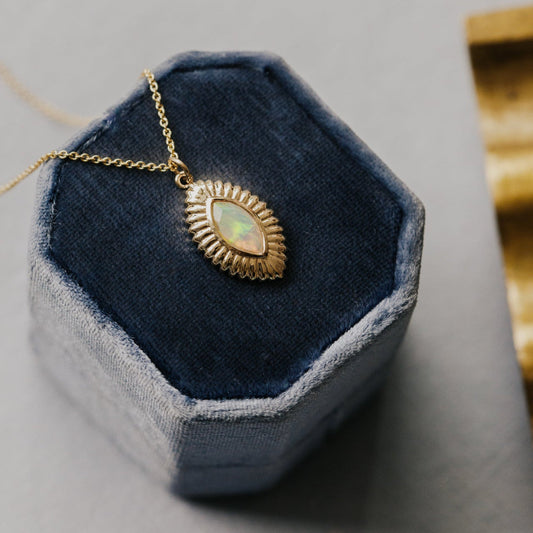Gold necklace with a opal pendant on a blue hexagonal jewelry display