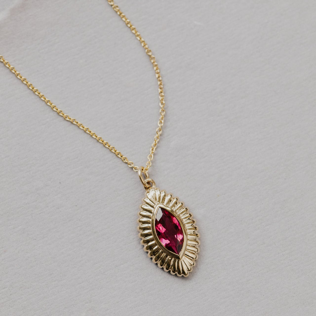 Gold necklace with a pink tourmaline gemstone pendant on a gray background
