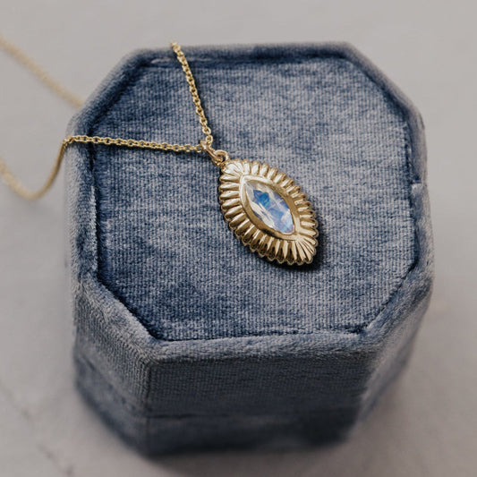 Gold necklace with a blue moonstone pendant on a textured blue surface