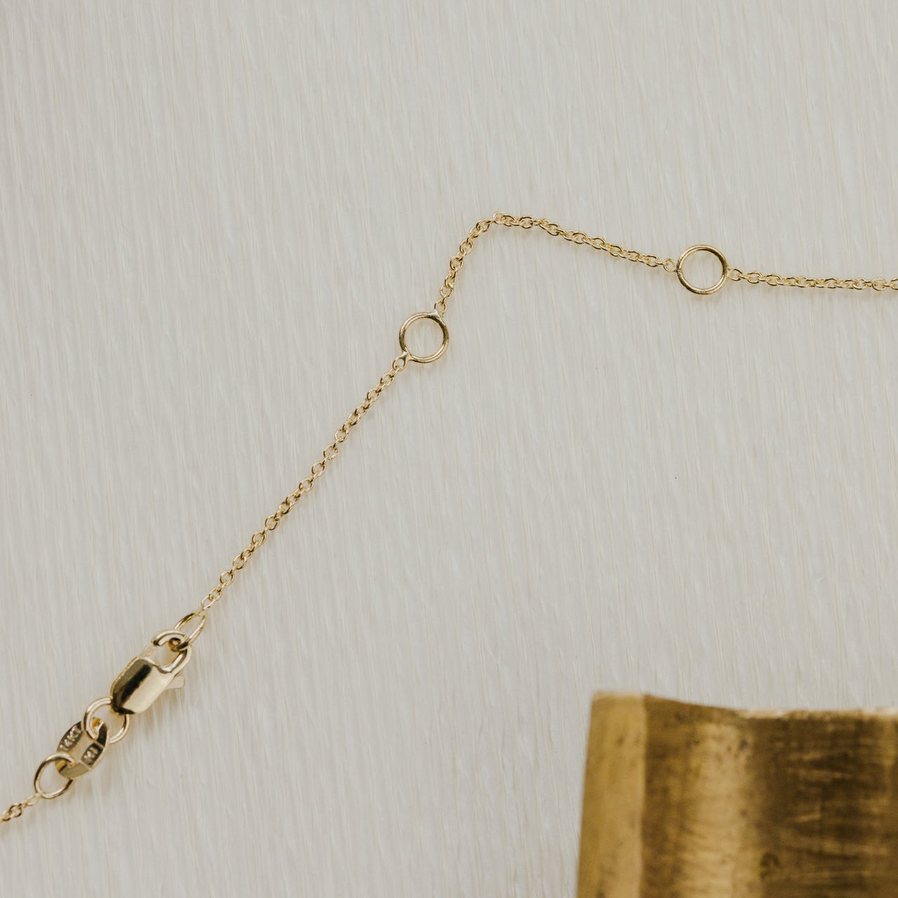 Gold necklace with clasp on a textured beige background