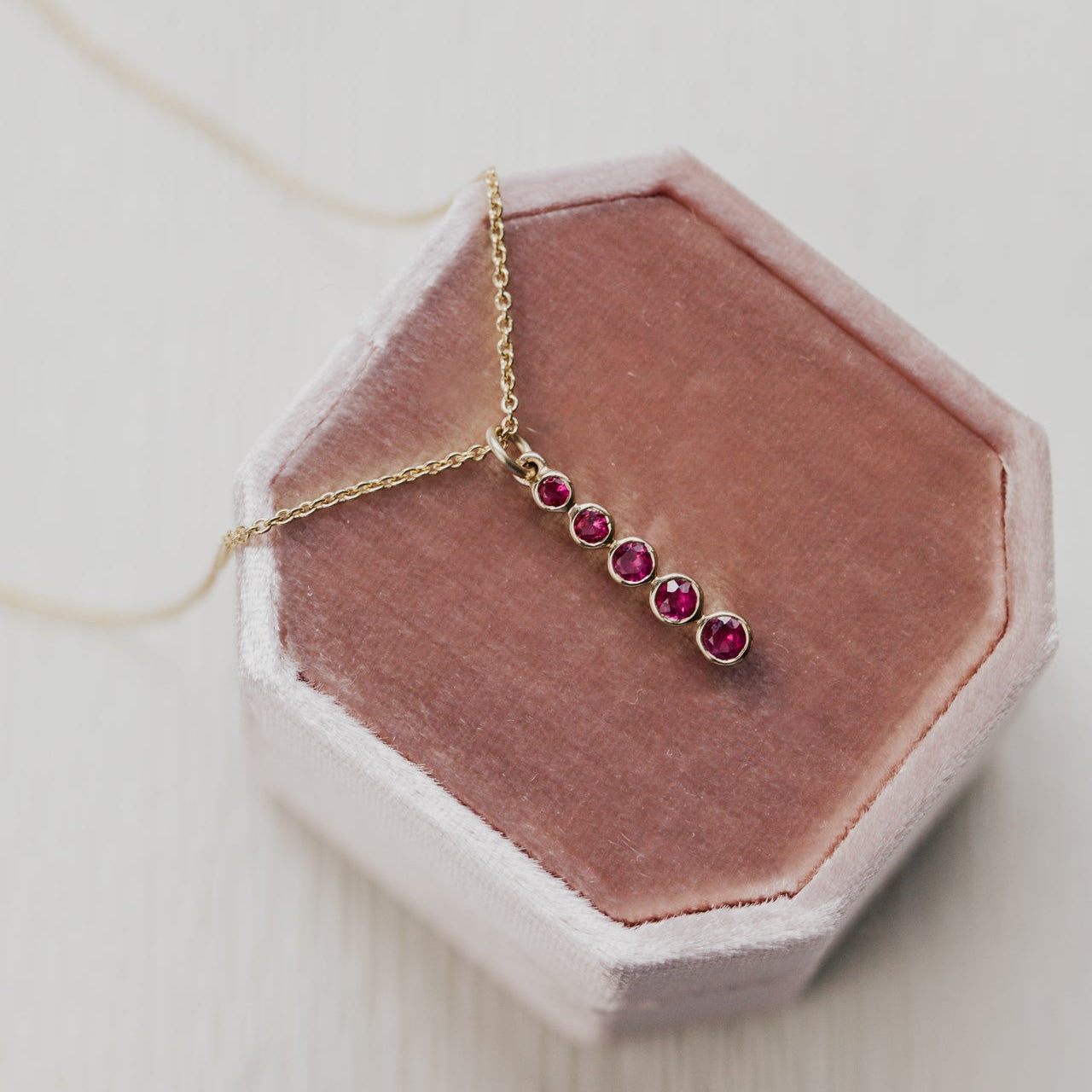 Gold necklace with red ruby gemstones on a pink hexagonal stand