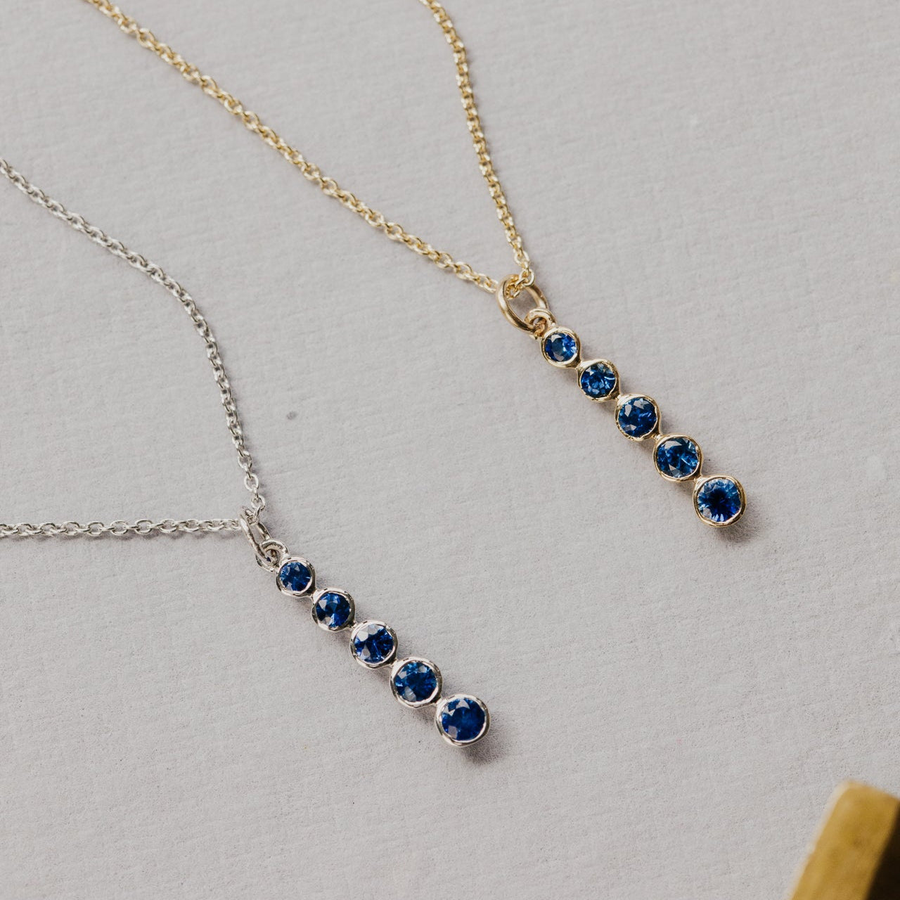 Two necklaces with blue sapphire gemstones on a light gray background