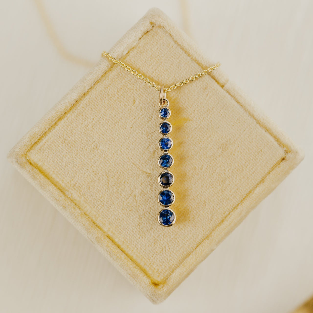 Gold necklace with blue sapphire  gemstones on a beige jewelry display box