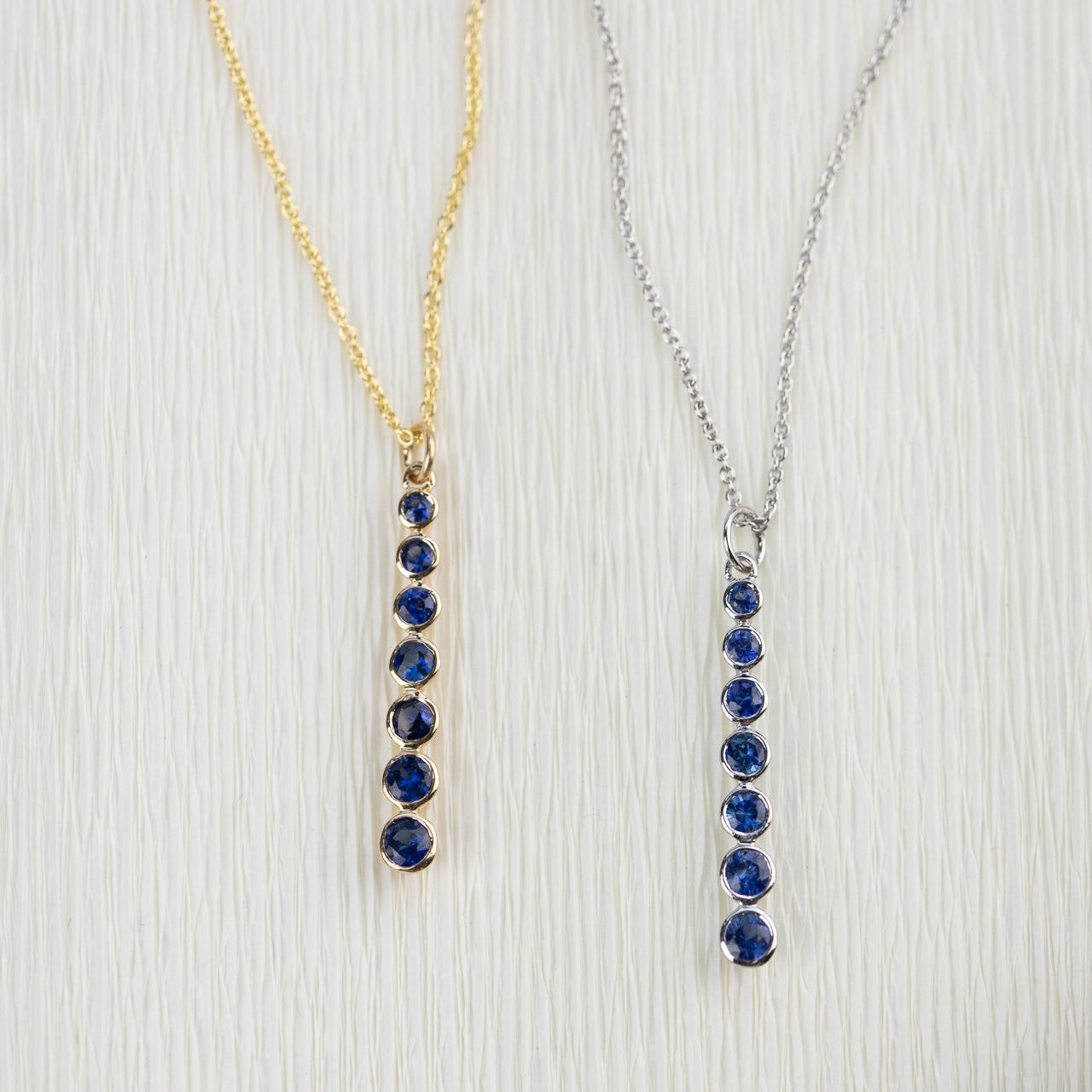 Two necklaces with blue sapphire gemstones on yellow and white gold chains against a light background