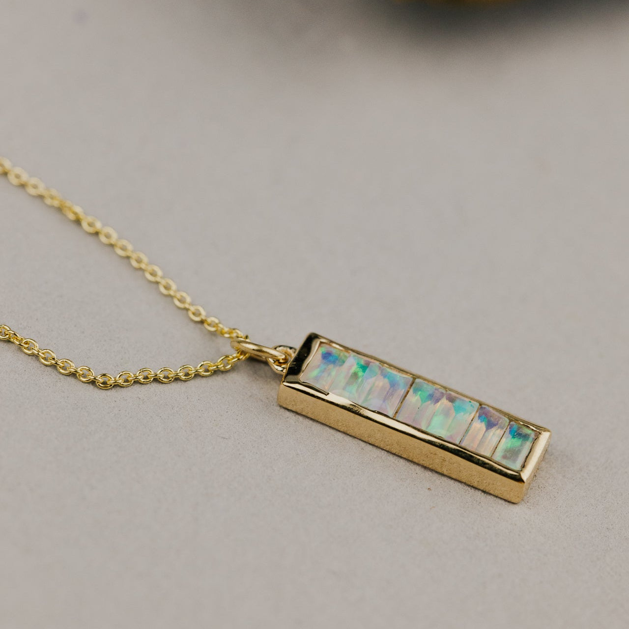 Gold necklace with a rectangular opal pendant on a light gray background