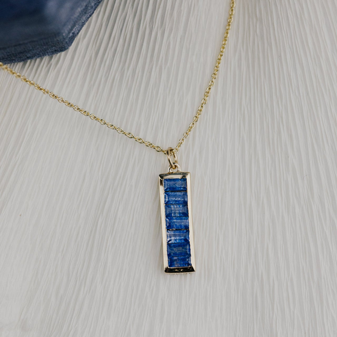 Gold necklace with a blue sapphire pendant on a textured surface