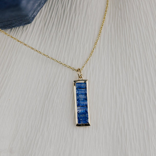 Gold necklace with a blue sapphire pendant on a textured surface