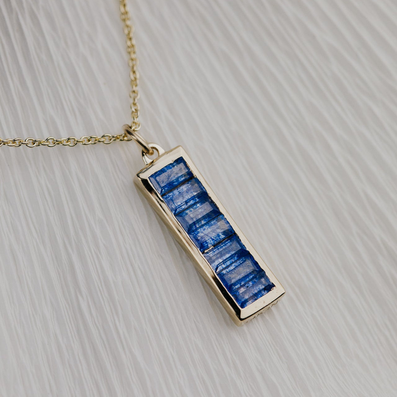 Gold necklace with a blue sapphire rectangular pendant on a light gray background