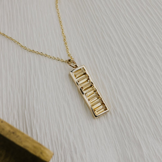 Gold necklace with a rectangular Citrine pendant on a light gray surface