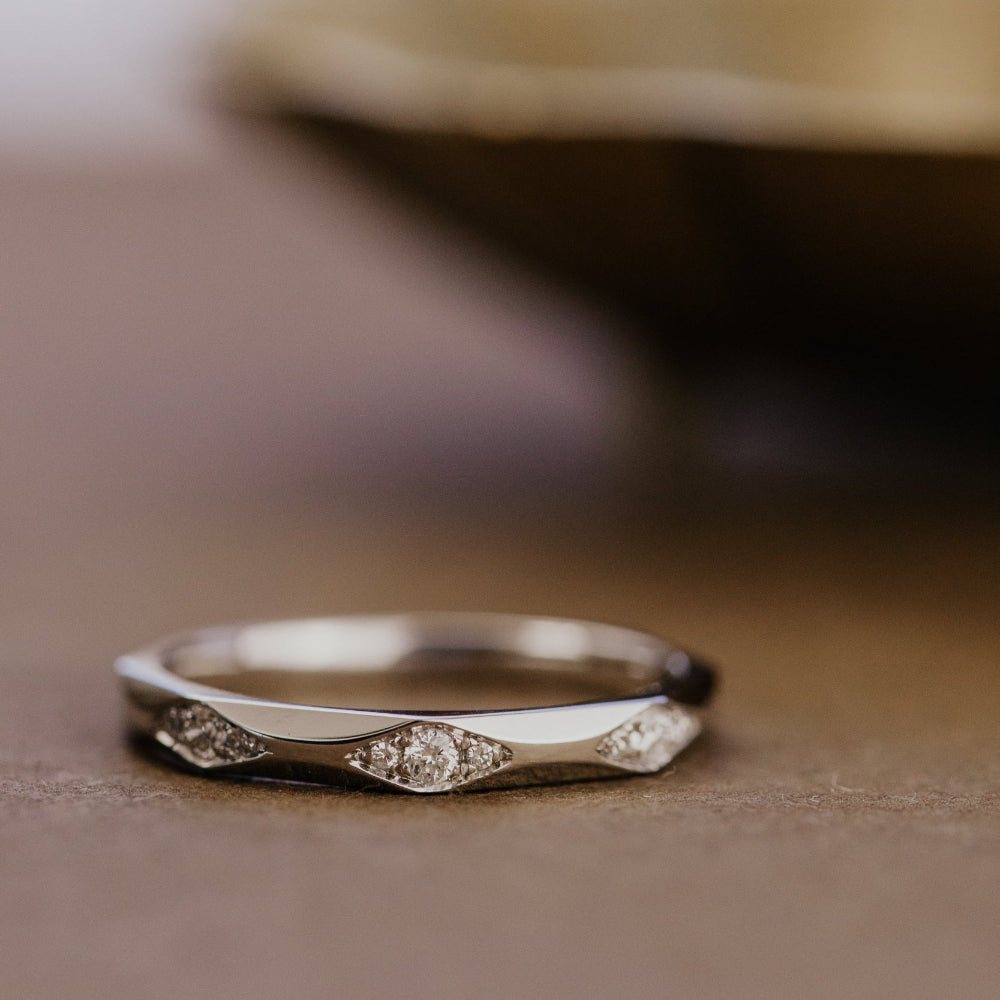 White gold wedding band with round diamonds on a wooden surface.