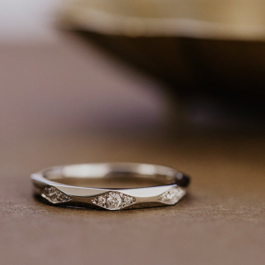 White gold wedding band with round diamonds on a wooden surface.