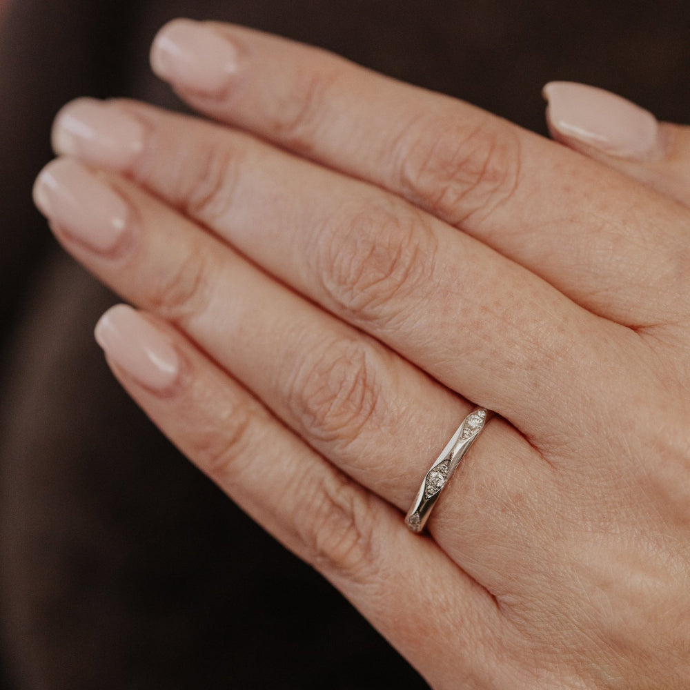 Hand wearing a white gold wedding band with round diamonds with a blurred background.